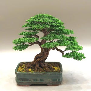 May include: A handcrafted bonsai tree sculpture. The tree features a detailed, twisted brown trunk and vibrant green wire foliage. It is planted in a rectangular, dark green ceramic pot. The bonsai is a unique piece of art.