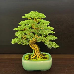 May include: A handcrafted bonsai tree sculpture. The tree features a twisted, textured trunk and vibrant green foliage, all meticulously crafted from wire. It is planted in a light green ceramic pot filled with green moss and dark soil.