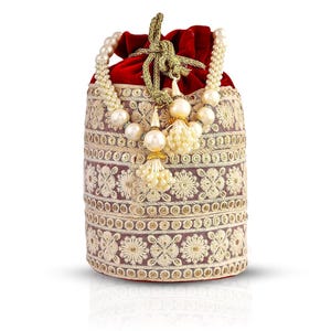 Puede incluir: Un bolso cilíndrico de terciopelo burdeos con intrincados bordados de color crema. El bolso presenta un cierre de cordón y está adornado con detalles de perlas y borlas. El asa es de perlas. El bolso está diseñado para ser un clutch o un bolso pequeño.