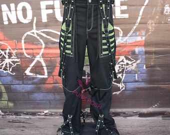 May include: Black cargo pants with green accents and straps. The pants have a unique design with multiple pockets and decorative elements. The background features graffiti art and the text "NO FUTURE".