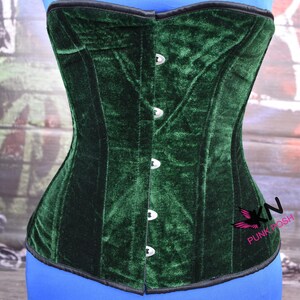 May include: A dark green velvet corset with a black trim and silver-colored clasps. The corset is displayed on a blue form. The brand logo "KN Punk Posh" is visible on the right side.