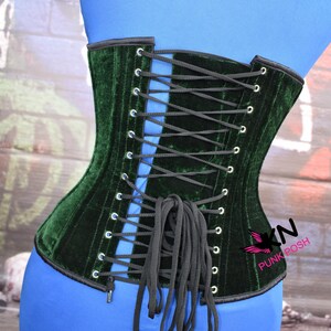 May include: A dark green velvet corset with black lacing. The corset is displayed on a blue form. The corset has a black trim and metal eyelets. The brand name "Punk Posh" is visible on the side.