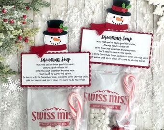 May include: A snowman-themed hot chocolate mix in a clear plastic bag with a red and white candy cane, white marshmallows, and chocolate candies. The bag has a red and white snowman design and the text "Snowman Soup" with instructions to add hot water and stir. The bag is labeled "Swiss Miss Milk Chocolate".