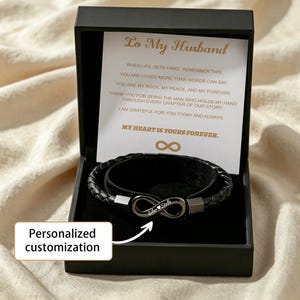 May include: A black braided leather bracelet with a metal infinity symbol clasp featuring the engraved names Silar and Stella. The bracelet is presented in a black gift box with a card containing the text To My Husband and a heartfelt message.