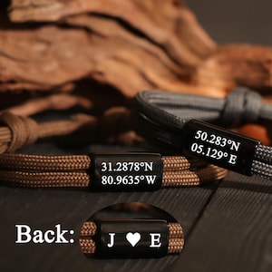 May include: Close-up of three personalized bracelets. One is brown, one is gray, and the third is brown. Each bracelet has a black rectangular clasp with engraved text: coordinates and initials. The text "Back: J ♥ E" is also visible.