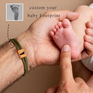 Puede incluir: Pulsera de cordón verde con un acento de madera con un diseño de huella de pie negro. La imagen incluye un pie de bebé y el texto "custom your baby Footprint".