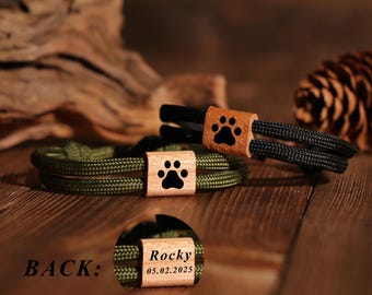 May include: Two rope bracelets with wooden accents. One bracelet is olive green, the other is black. Each has a wooden accent with a black paw print. The back of one bracelet is engraved with the name "Rocky" and the date "05.02.2025".