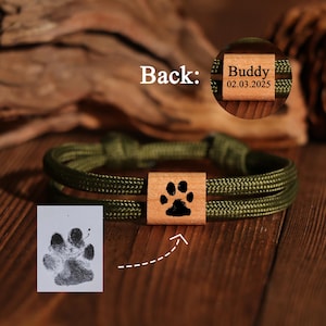 Peut inclure: Bracelet en corde vert olive avec un carré en bois orné d'une empreinte de patte noire. Le dos du carré en bois porte le nom "Buddy" et la date "02.03.2025". Une empreinte de patte est affichée sur papier blanc.