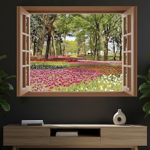 Puede incluir: Una ventana con marco de madera y contraventanas abiertas revela una vibrante escena de jardín. El jardín presenta hileras de coloridos tulipanes en tonos rosa, rojo, naranja y blanco, con un telón de fondo de árboles verdes y cielo azul. Un jarrón decorativo está sobre un mueble de madera.
