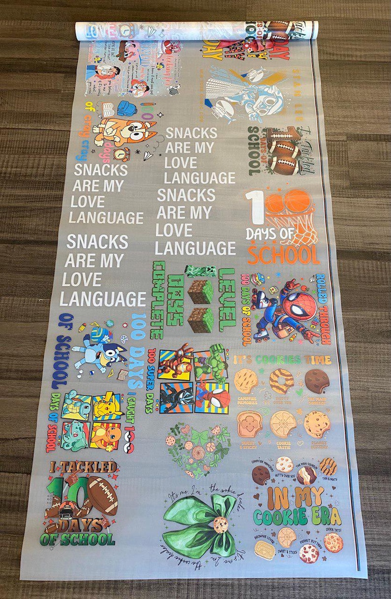 May include: A gray fabric banner with colorful illustrations and text. The banner features cartoon characters, cookies, and phrases like "Snacks are my love language" and "100 days of school".