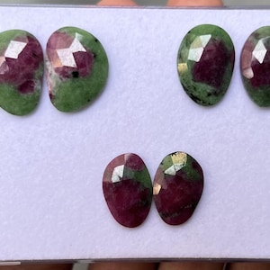 Peut inclure: Six pierres précieuses facettées aux couleurs variées. Les gemmes sont de forme ovale, avec un centre rouge foncé et des bords verts. Les gemmes sont présentées sur une surface blanche.
