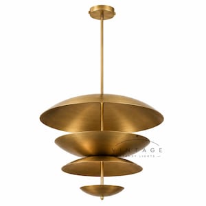 May include: A brass pendant light fixture featuring four stacked, bowl-shaped discs of varying sizes suspended from a central vertical rod. The metal has a brushed finish. The text VINTAGE STANDY LIGHTS is printed in black on the second disc from the top.