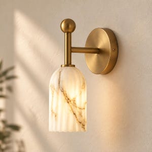 Peut inclure: Une applique murale composée d'une plaque de montage circulaire en laiton brossé et d'un bras vertical surmonté d'un embout sphérique. Le luminaire comprend un abat-jour en verre blanc translucide cannelé avec des veines brunes.