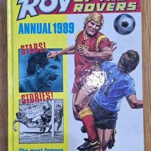 Peut inclure: Couverture d'un album annuel "Roy of the Rovers" de 1989. L'illustration dynamique montre des joueurs de football en action, avec un ballon de football en arrière-plan. La couverture est jaune avec du texte rouge et bleu.
