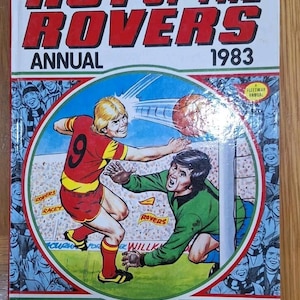 Peut inclure: Couverture d'un album annuel "Roy of the Rovers" de 1983. L'illustration colorée représente un match de football avec deux joueurs en action. Le titre est en rouge, avec le texte "Top of the League for Football!"