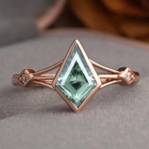 May include: Rose gold ring featuring a kite-shaped, light green gemstone. The ring has a delicate design with small diamond accents on each side of the band. The gemstone is the focal point, set in a geometric, modern style.