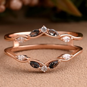 May include: A rose gold ring guard featuring two curved bands connected at the sides. The bands are adorned with marquise-cut rutilated quartz stones and small round white diamonds, creating a symmetrical V-shaped design on both the top and bottom.