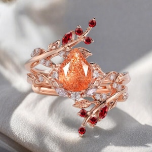 Puede incluir: Anillo de oro rosa con una gran gema naranja en forma de pera. El anillo presenta un diseño floral con piedras de acento rojas y claras. La banda se envuelve alrededor del dedo en espiral.
