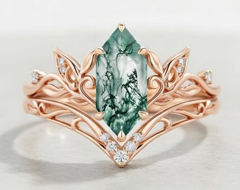 Peut inclure: Une bague en or rose avec une pierre centrale en agate mousse taille marquise aux inclusions vert foncé. L'anneau présente des motifs complexes de feuilles et de vignes en métal, agrémentés de petites pierres blanches rondes serties.