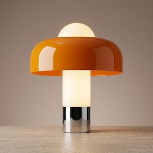 May include: A modern table lamp with a vibrant orange shade and a white, cylindrical base. The lamp features a chrome-colored base and a small, spherical white light on top. The design is sleek and contemporary.