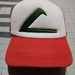 May include: A red and white baseball cap with a green embroidered design. The cap features a red brim and a white mesh back. The green design is a stylized letter "A".