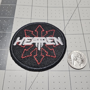 May include: A circular black embroidered patch featuring a red eight-pointed star symbol and the white text HEATHEN centered across the middle. The patch is positioned next to a United States quarter coin for scale, showing its relative size.