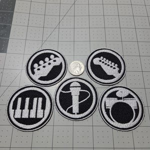 May include: Five circular embroidered patches featuring white musical icons on a black background, including a guitar headstock, piano keys, a microphone, and a drum set. A US quarter coin is placed in the center for scale reference.