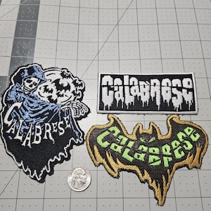 May include: Three embroidered patches featuring the word Calabrese. One patch shows a skeleton in a blue cloak with a moon, one is a rectangular black patch with white text, and one is a bat-shaped patch with green text and gold trim, next to a US quarter.