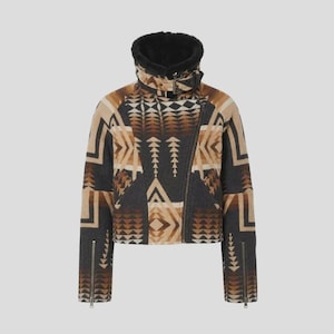 Op de afbeelding: Een kort jasje met een geometrisch patroon in donkergrijs, bruin en beige. Het jasje heeft een hoge kraag gevoerd met zwarte imitatiebont, een asymmetrische ritssluiting aan de voorzijde, een gespsluiting bij de hals en lange mouwen met ritsen.