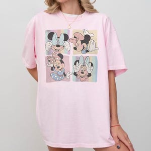 Puede incluir: Una camiseta rosa claro con un gr&aacute;fico de cuatro paneles de Minnie Mouse en varias poses. Cada panel tiene un fondo pastel. La camiseta tiene un corte holgado y de gran tama&ntilde;o.