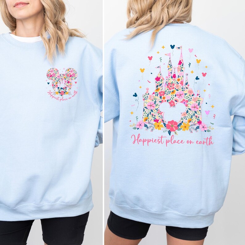 May include: Light blue sweatshirt featuring a floral Mickey Mouse design on the front and a floral castle on the back. The text "Happiest place on earth" is printed on both sides in pink.