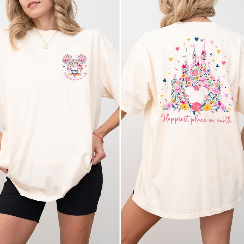 May include: Cream-colored t-shirt featuring a floral Mickey Mouse design on the front and a floral castle design on the back. The text "Happiest place on earth" is printed on both sides of the shirt. The shirt has short sleeves.