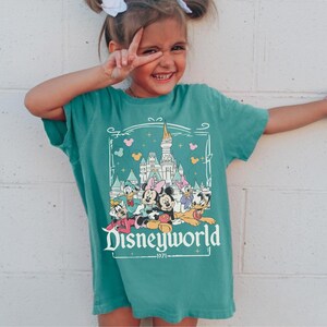 May include: Teal t-shirt featuring a Disneyworld graphic with Mickey, Minnie, Donald, Daisy, and Goofy in a castle scene. The graphic includes the text "Disneyworld" and the year "1971".
