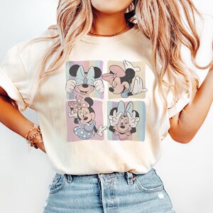 Puede incluir: Camiseta color crema con un dise&ntilde;o pop art colorido de Minnie Mouse en cuatro poses diferentes. Cada cuadrado muestra a Minnie con un lazo y una expresi&oacute;n diferentes, sobre fondos pastel.