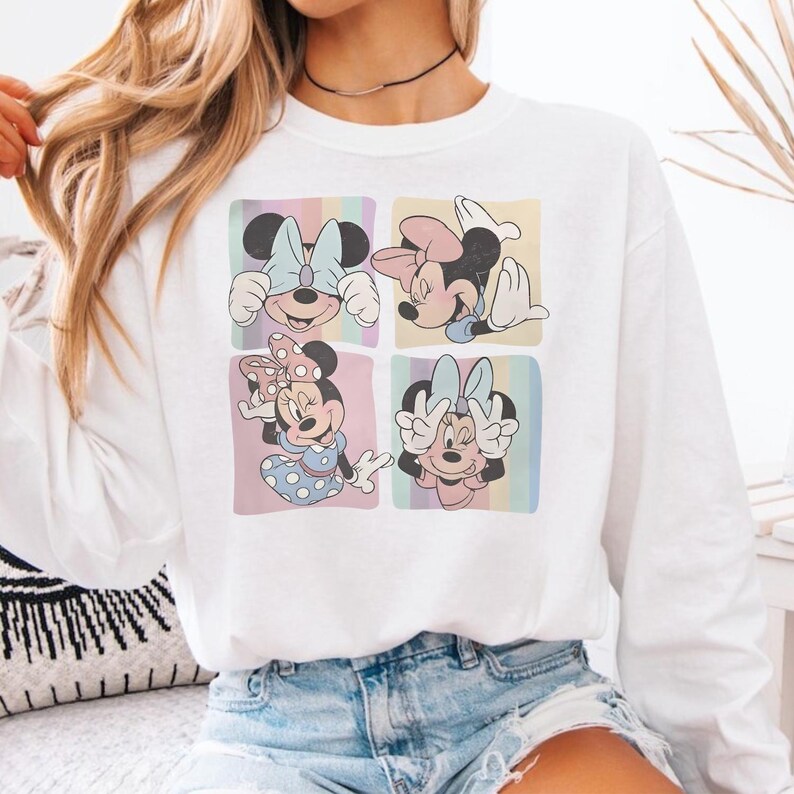 Puede incluir: Sudadera blanca con cuatro paneles que muestran ilustraciones de Minnie Mouse. Cada panel muestra una pose diferente de Minnie Mouse sobre un fondo pastel. La sudadera es de cuello redondo y manga larga.