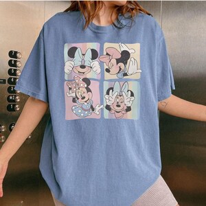 Puede incluir: Camiseta azul claro con cuatro cuadrados que muestran diferentes dise&ntilde;os de Minnie Mouse. Los cuadrados tienen fondos pastel. Minnie aparece con lazos y vestidos. La camiseta tiene un corte holgado y extragrande.