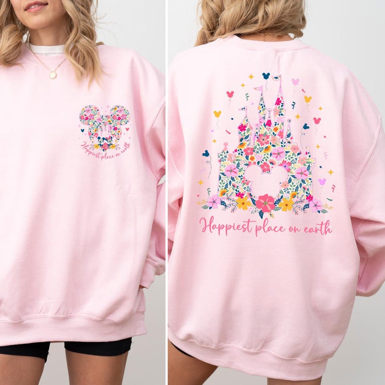 May include: A light pink sweatshirt with a floral Mickey Mouse design on the front and a floral castle design on the back. The text "Happiest place on earth" is printed on both sides of the sweatshirt.