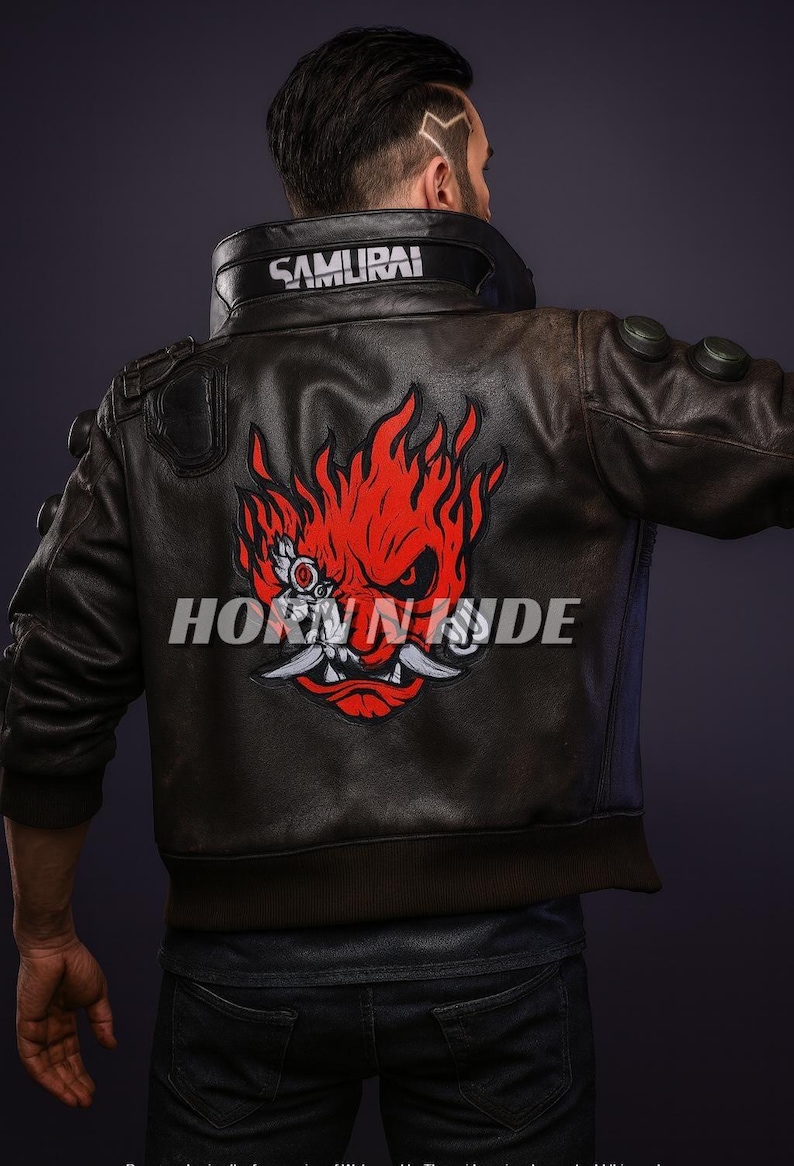 Pu&ograve; includere: Giacca di pelle marrone con grafica rossa e bianca sul retro. La giacca ha la scritta "SAMURAI" sul colletto e il testo "HORN N HIDE" sul retro. La giacca &egrave; indossata da una persona.