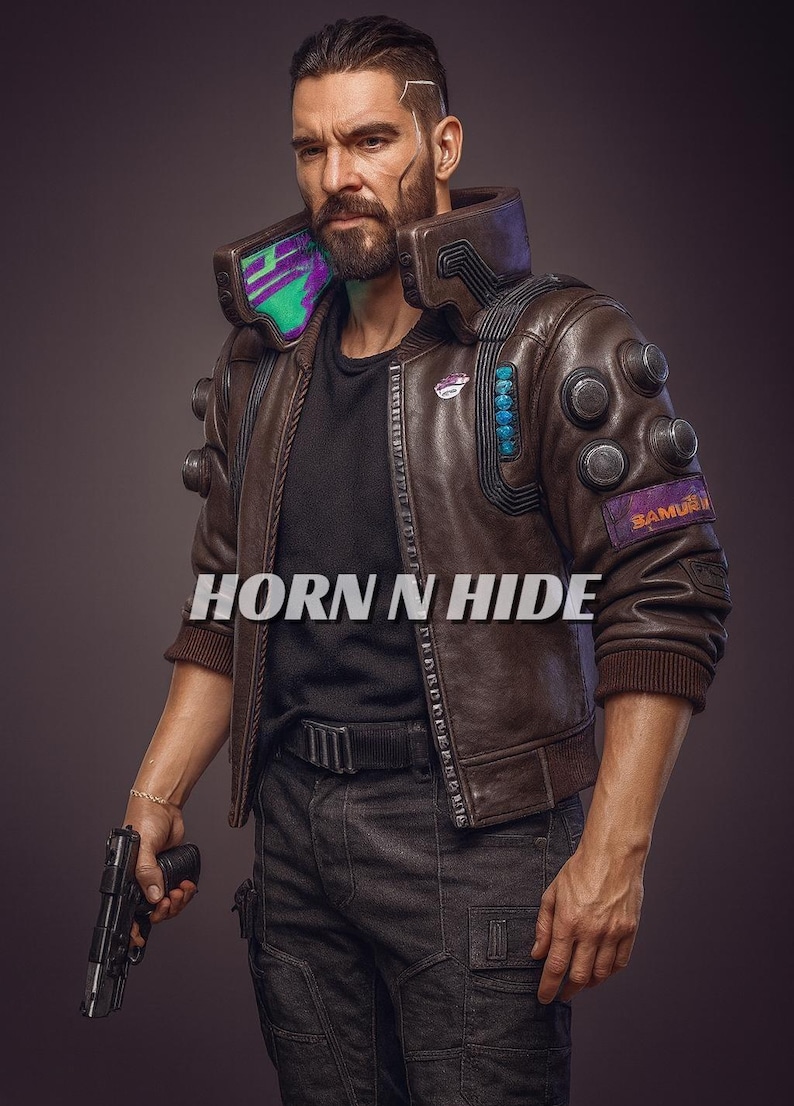 Pu&ograve; includere: Giacca di pelle marrone con colletto alto e molteplici elementi decorativi. La giacca presenta una toppa "SAMURAI" e il testo "HORN N HIDE" &egrave; visibile. La persona tiene in mano una pistola nera.