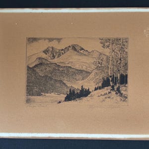 May include: A rectangular framed print featuring a black and white ink drawing of a mountain range. The landscape includes a dense forest in the foreground, a valley, and tall trees on the right side. The artwork is centered on a tan mat board.