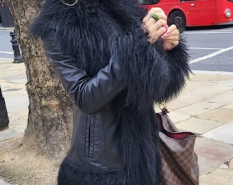 May include: A black leather jacket with long, shaggy black fur trim around the collar, cuffs, and hem. The jacket has a tailored fit and a classic design. A brown and tan checkered tote bag is visible.