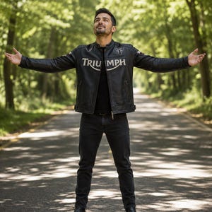 May include: A black leather motorcycle jacket featuring the word TRIUMPH in large white lettering across the chest, a small white logo on the upper left side, a stand-up collar, a full-length front zipper, and adjustable side waist straps.