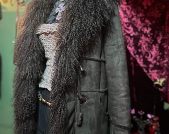 May include: A dark green coat with a long, shaggy, dark brown fur collar and trim. The coat has toggle closures and pockets. A mannequin head is wearing a silver cross pendant with a purple stone.