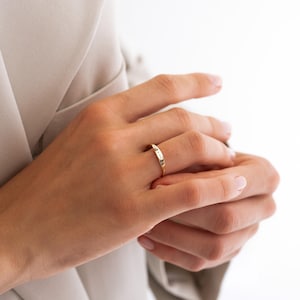 Puede incluir: Un anillo de oro con una cara rectangular adornada con peque&ntilde;as piedras claras. El anillo se lleva en un dedo, sobre un fondo neutro. El dise&ntilde;o del anillo es sencillo y elegante, adecuado para el uso diario.