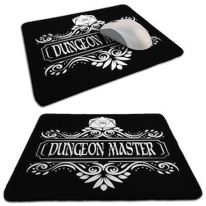 May include: Black mouse mat featuring the words "DUNGEON MASTER" in white, decorative lettering. A white computer mouse rests on the mat. The design includes a white die and floral accents, ideal for tabletop gaming.