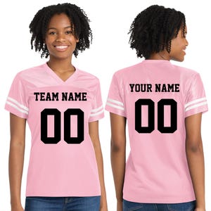 Może przedstawiać: R&oacute;żowa koszulka do futbolu z białymi paskami na rękawach. Prz&oacute;d koszulki zawiera napis "TEAM NAME" nad czarnym numerem "00". Tył koszulki zawiera napis "YOUR NAME" nad czarnym numerem "00".