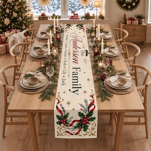 Könnte beinhalten: Ein langer, cremefarbener Tischläufer aus Stoff mit festlichem Weihnachtsmotiv aus Stechpalmenblättern, roten Beeren und goldenen Verzierungen. Der Text lautet The Anderson Family, gefolgt von den Namen Michael, Sarah, Emma, Noah, Lily und Jack.