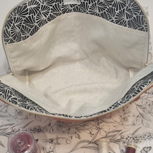 Può includere: Borsa tote aperta con fodera a motivo a ventaglio bianco e nero che borda il bordo superiore e le tasche interne. L'interno della borsa è di colore chiaro. Sono visibili forniture per cucito, tra cui rocchetti di filo e un cuscinetto per spilli.