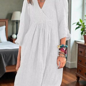 K&ouml;nnte beinhalten: Wei&szlig;es V-Ausschnitt-Kleid mit Dreiviertel&auml;rmeln. Das Kleid hat eine geraffte Taille und eine lockere Passform. Die &Auml;rmel sind leicht gepufft. Das Kleid ist aus leichtem Stoff gefertigt, ideal f&uuml;r warmes Wetter.