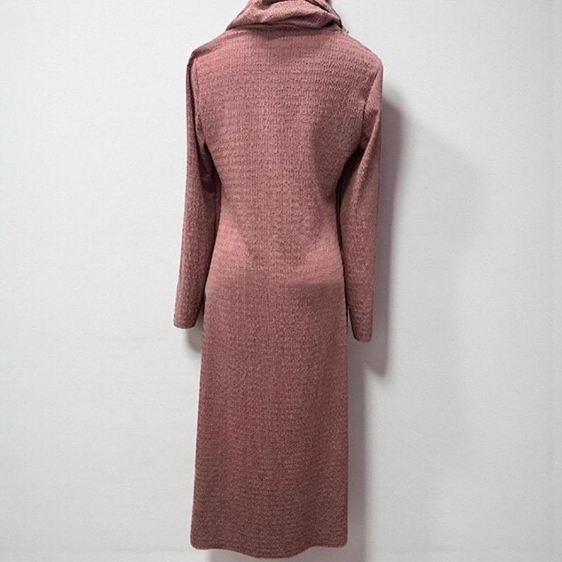 May include: A long, mauve-colored dress with a textured knit fabric. The dress features long sleeves and a cowl neck. The garment is floor-length and has a simple, elegant design, suitable for various occasions.